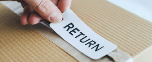 Hand placing white return label with black text onto corrugated cardboard box for e-commerce return shipping