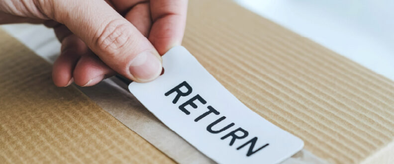 Hand placing white return label with black text onto corrugated cardboard box for e-commerce return shipping