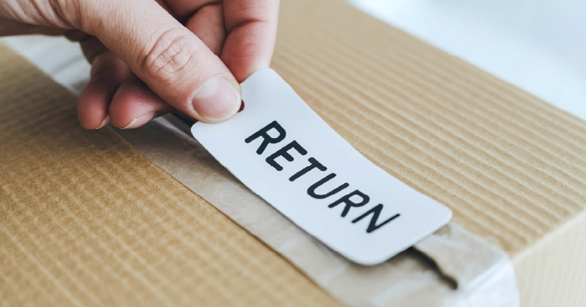 Hand placing white return label with black text onto corrugated cardboard box for e-commerce return shipping